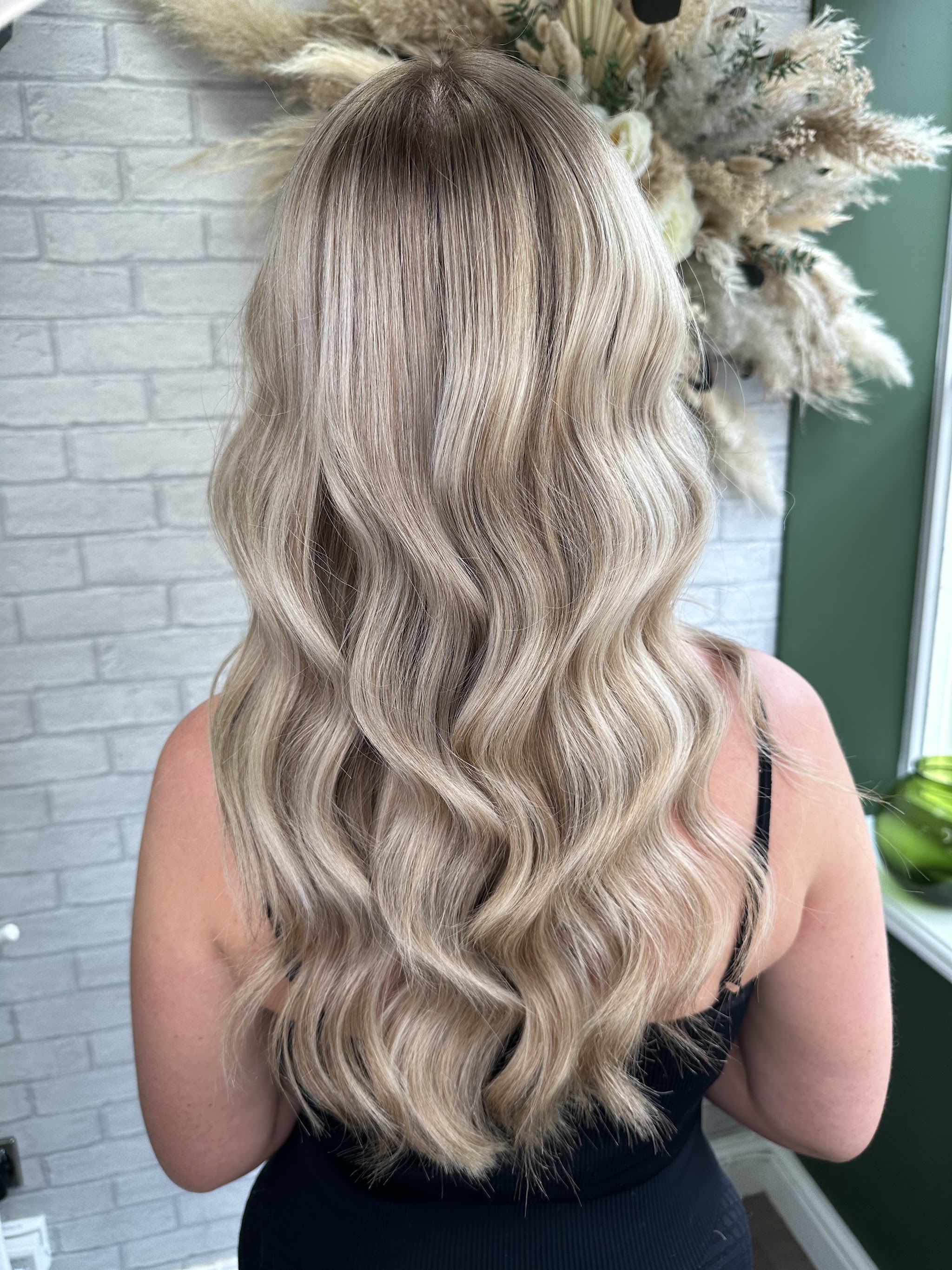 Blonde balayage waves in front of the studio’s dried flower display